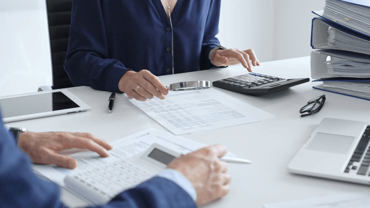 Two professionals reviewing tax documents with a magnifying glass and calculator during a tax audit meeting