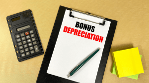 Bonus depreciation explained on clipboard with calculator and notepad