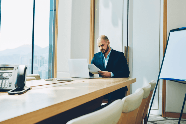 Section 179 vs bonus depreciation – businessman reviewing tax documents at a conference table with a laptop in a high-rise office