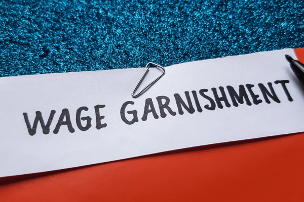 Wage garnishment note with paper clip and pen on red and teal background