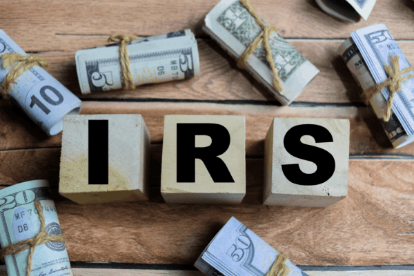 Wooden blocks spelling IRS surrounded by rolled cash bills representing federal wage garnishment limits IRS enforces on taxpayers