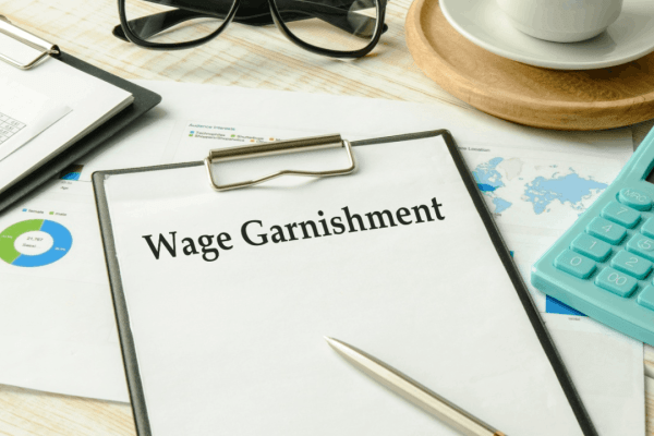 Wage garnishment document on clipboard with calculator and financial charts on desk