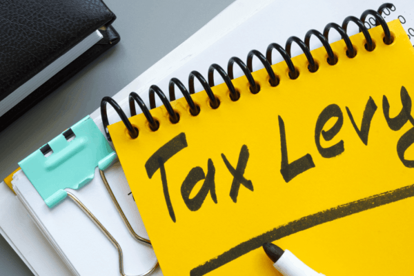 Tax levy written on yellow notepad with financial documents and binder clip on desk